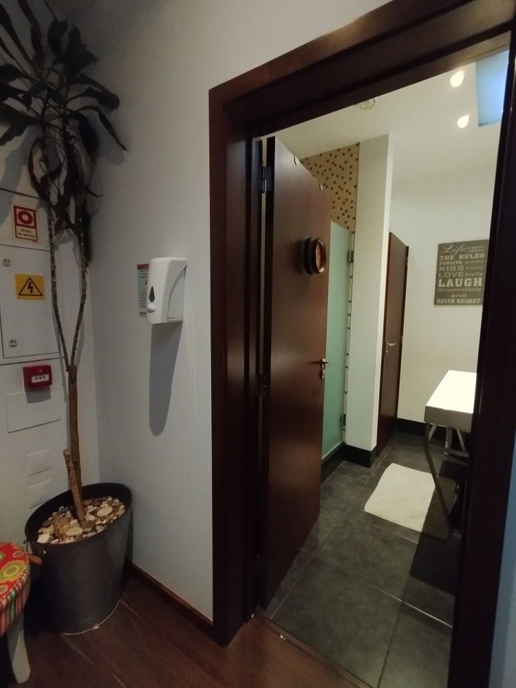 Hallway entrance to a restroom with open dark wood door, white walls, and a floor mat inside