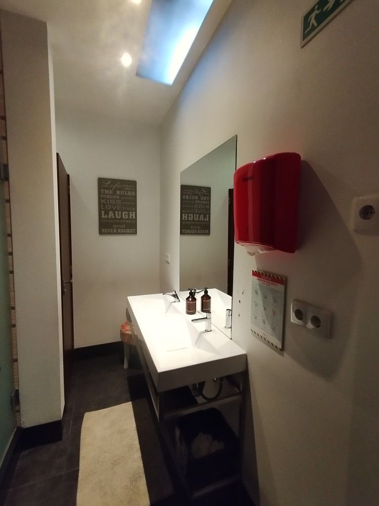 Small restroom with white sink, mirror, red towel, and wall signs under bright overhead light