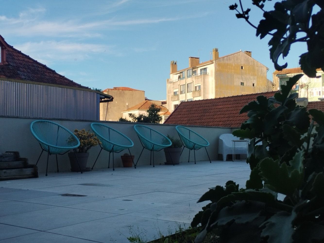 Rooftop patio with turquoise chairs, white tiles, and surrounding city buildings at sunset.