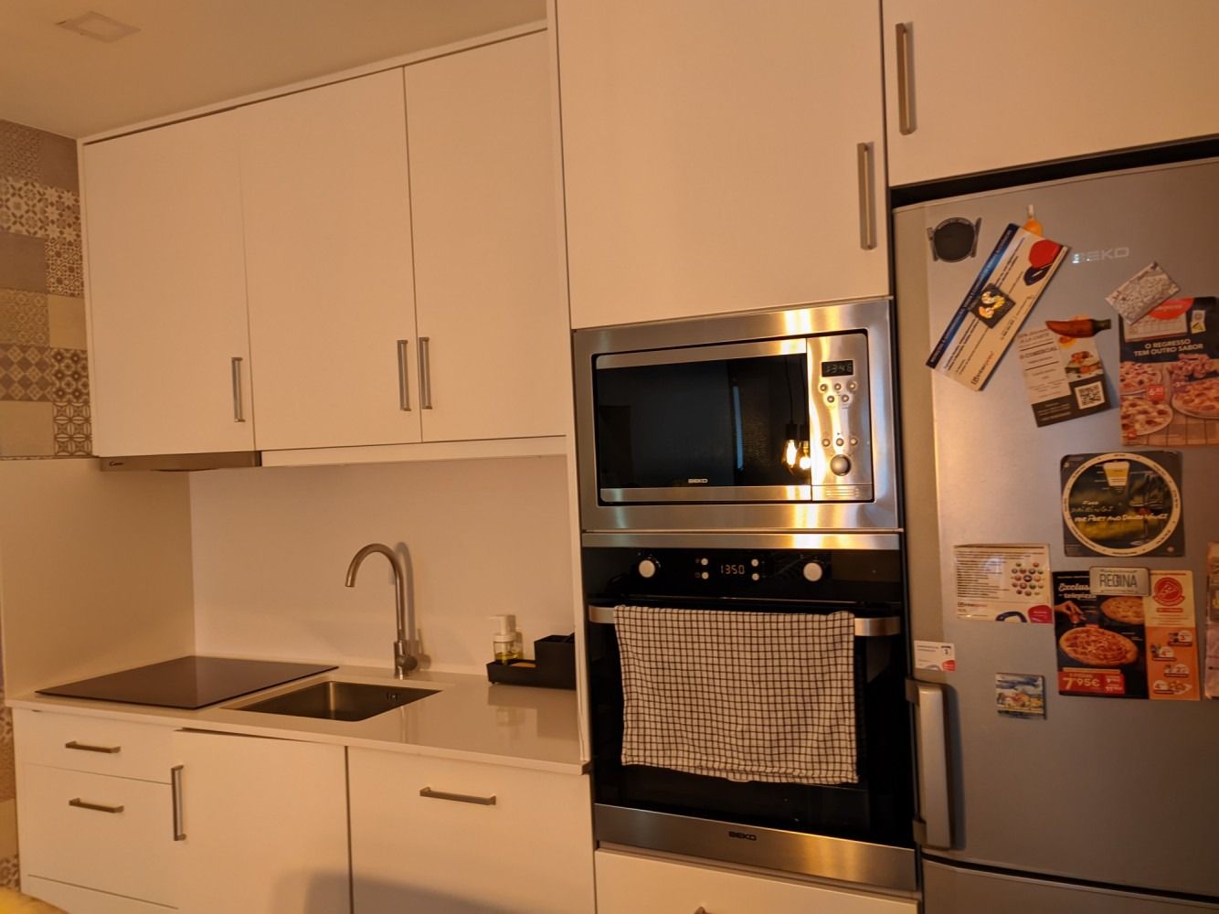 Compact kitchen with white cabinets, stainless steel oven and fridge, and a sink under a countertop.
