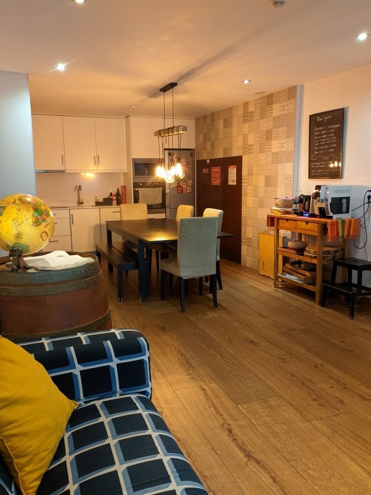 Cozy open-plan kitchen and dining area with wooden floors, pendant lights, blue chair, and rolling cart.