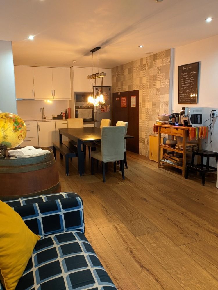 Cozy open-plan dining room and kitchen with wooden floor, pendant lights, and blue patterned sofa.