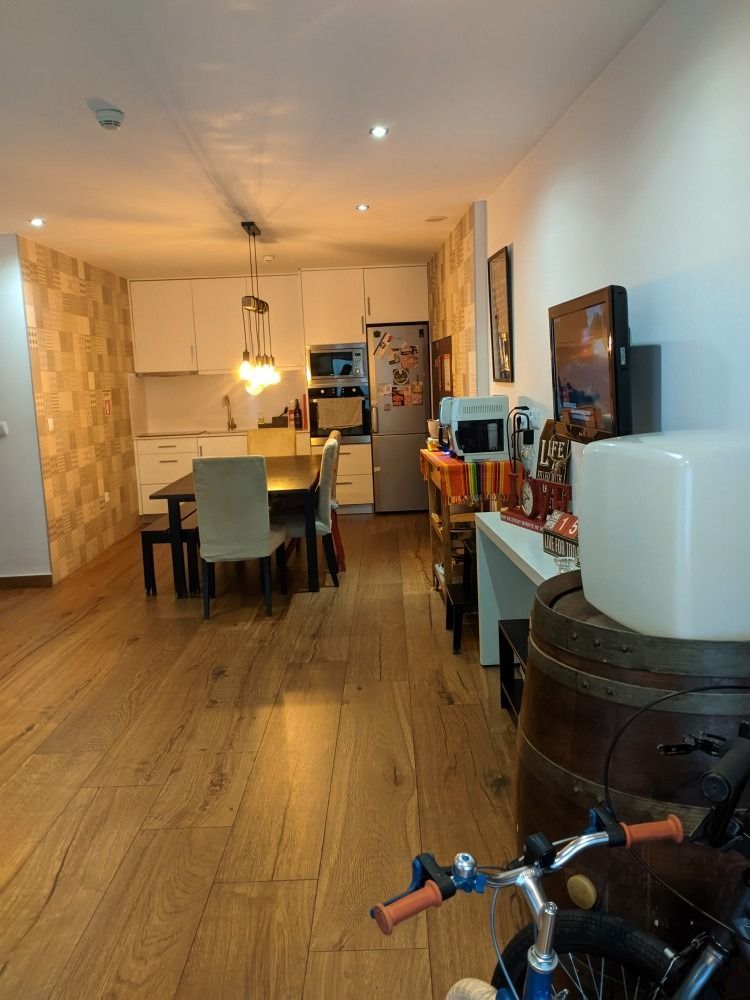 Modern dining and living area with wooden floors, table, TV, and decorative lights