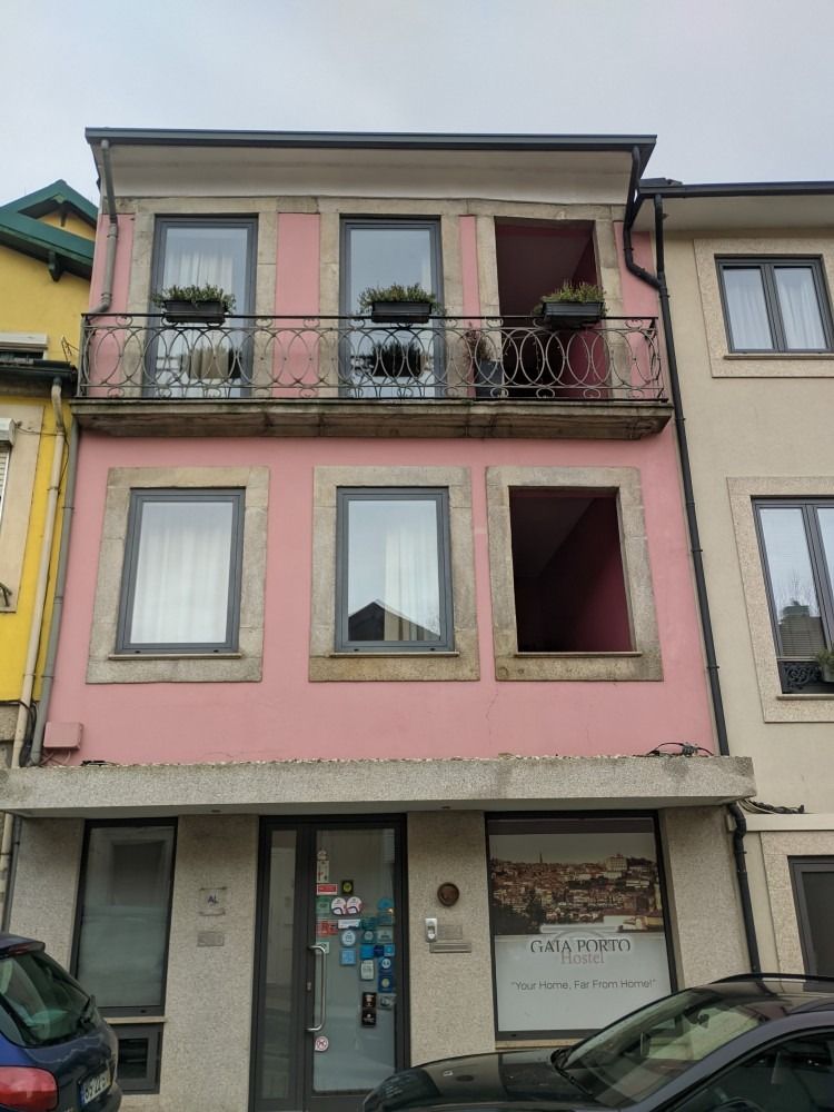Three-story pink storefront building with balconies and parked cars on the street