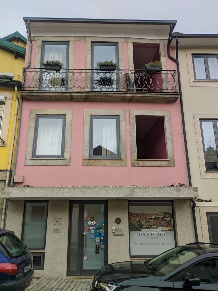 Three-story pastel building with balconies and storefront windows on a street, with parked cars in front.