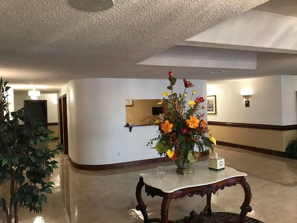 Hotel lobby with a curved reception desk, marble table with flowers, and glossy floors.