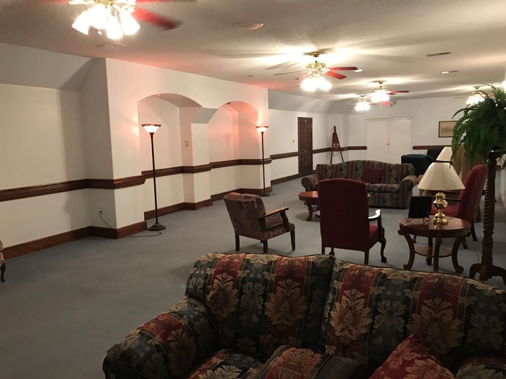 Spacious room with couches and chairs. Neutral walls, recessed arches, and dim lighting.