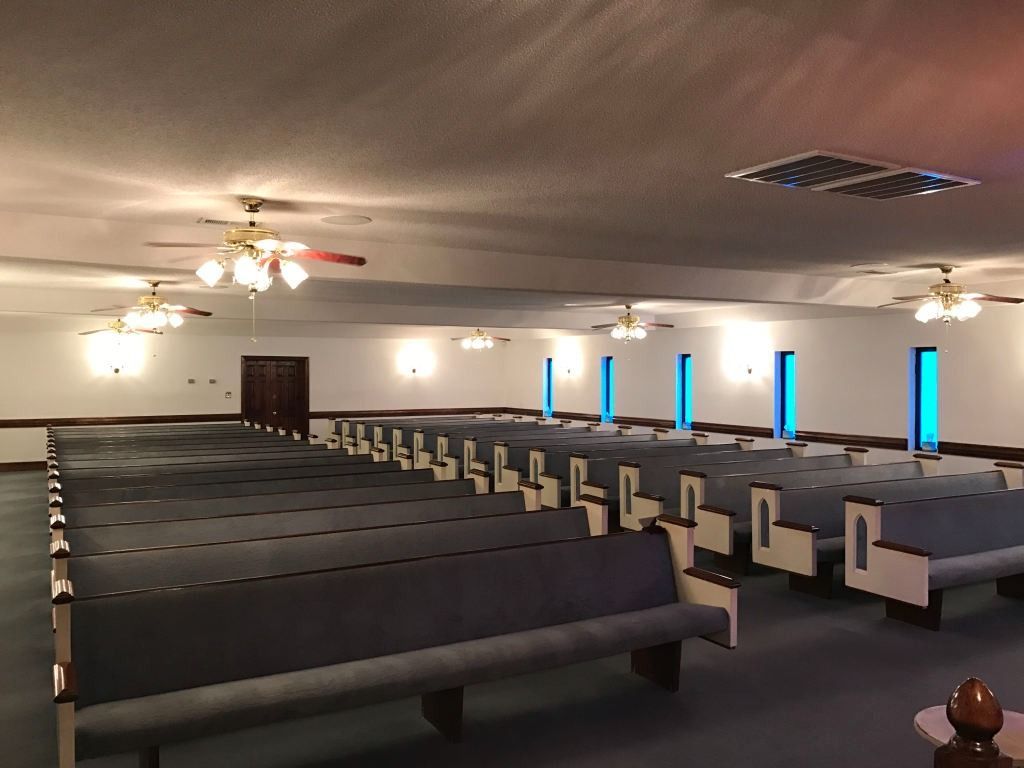 Empty church sanctuary with rows of pews, ceiling fans, and blue-tinted windows.