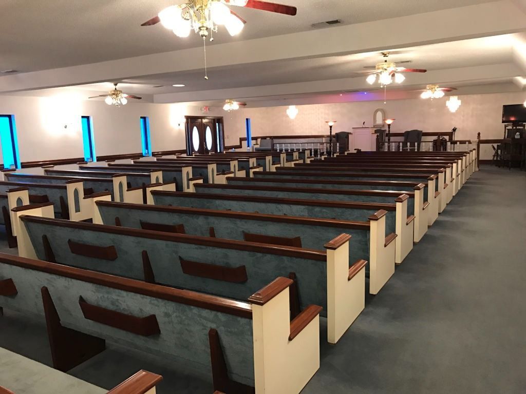 Empty church sanctuary with rows of pews, blue carpet, and stained glass windows.