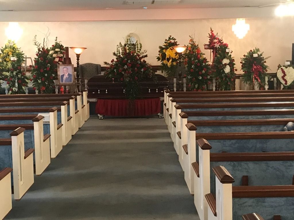 Funeral service in a church. Brown casket surrounded by floral arrangements, rows of pews.