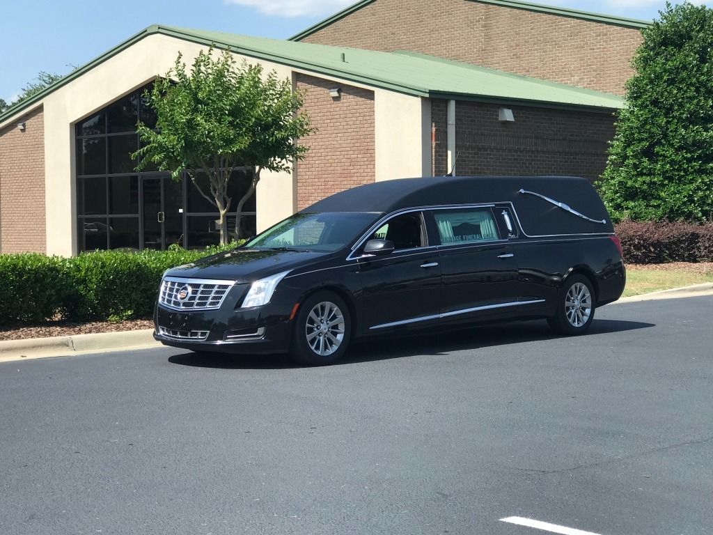 Black hearse parked outside a building with large windows and a green roof.