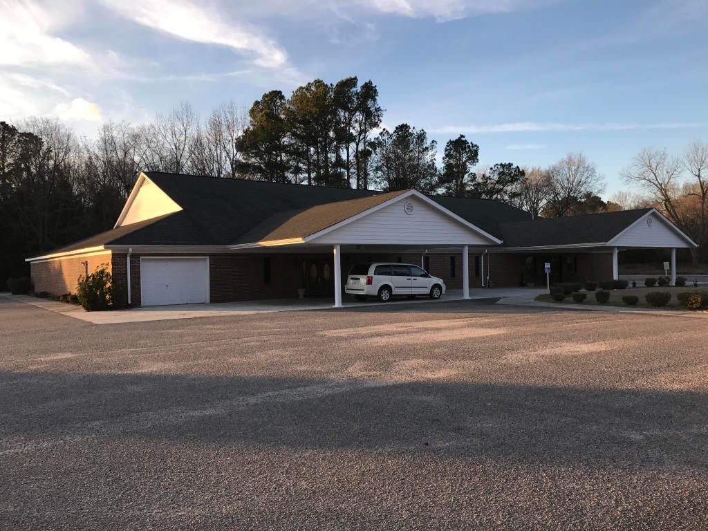 Brick building with covered parking; gravel lot. Trees in the background. Cloudy sky.