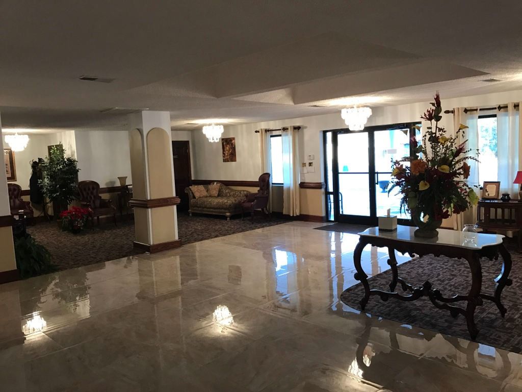 Lobby with shiny tiled floor, seating areas, large floral arrangement, and glass doors.