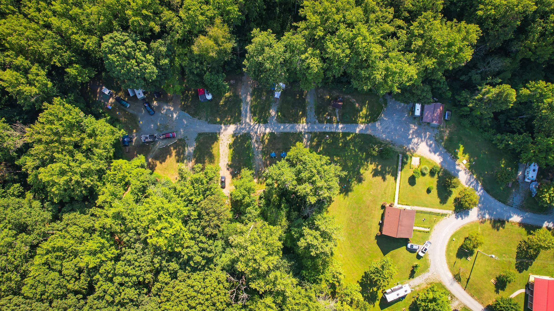 Aerial view of a campsite with a dirt road, surrounded by green trees, and a few buildings and campers.