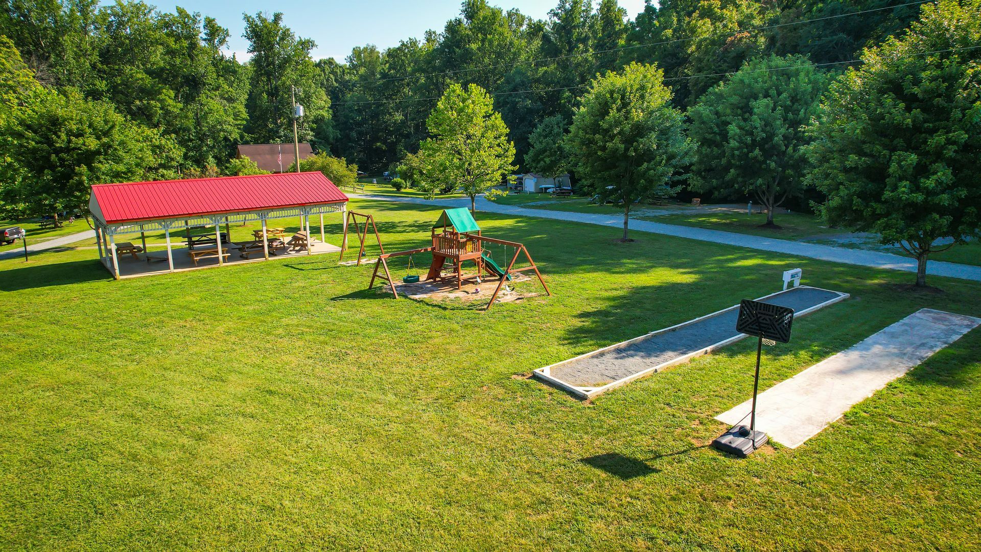 Park with a red-roofed shelter, playground, lawn area, and paved walkways, surrounded by green trees.