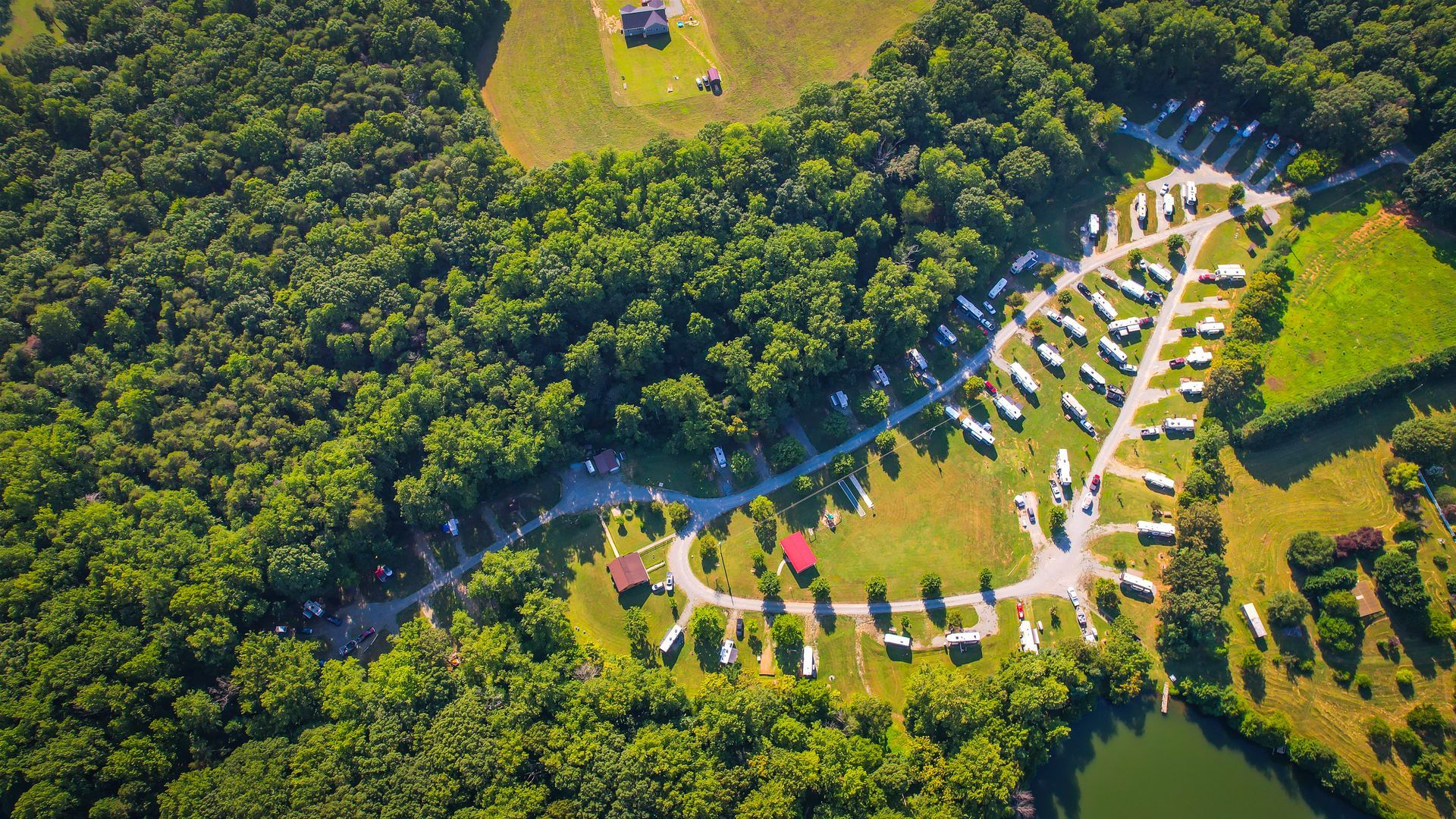 Aerial view of RV campground nestled between a forest and grassy fields.