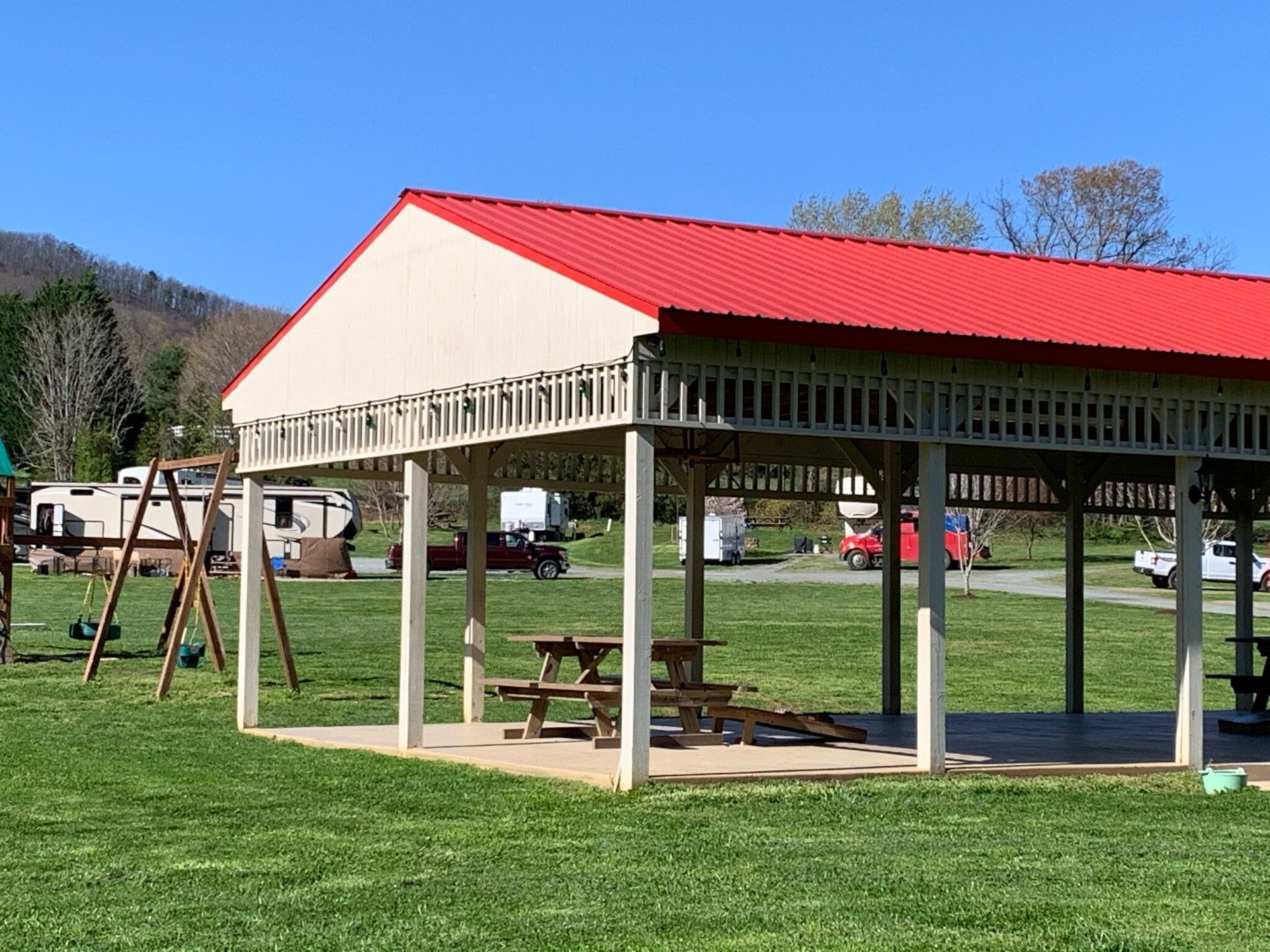 Picnic shelter with red roof, picnic tables, and RVs in a grassy field.