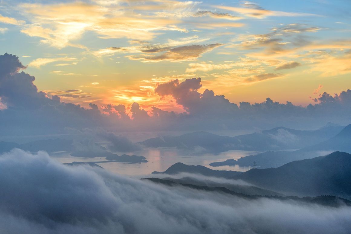 Sunset over mountain range and misty lake; orange and blue hues.