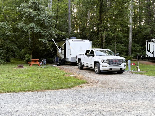 RV parked on green grass in a campground, with a picnic table and surrounding trees.