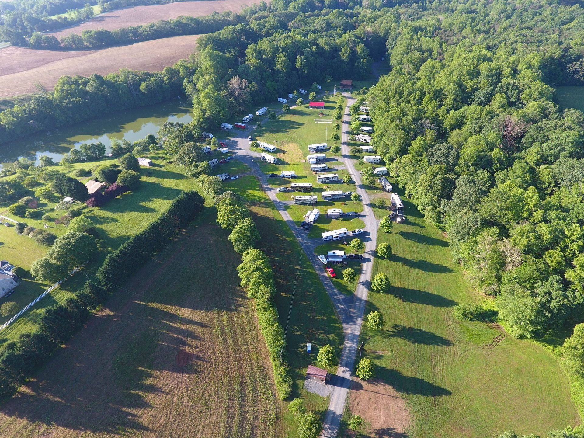 Aerial view of a campground with RVs and trailers lined up along a road, surrounded by trees and fields.