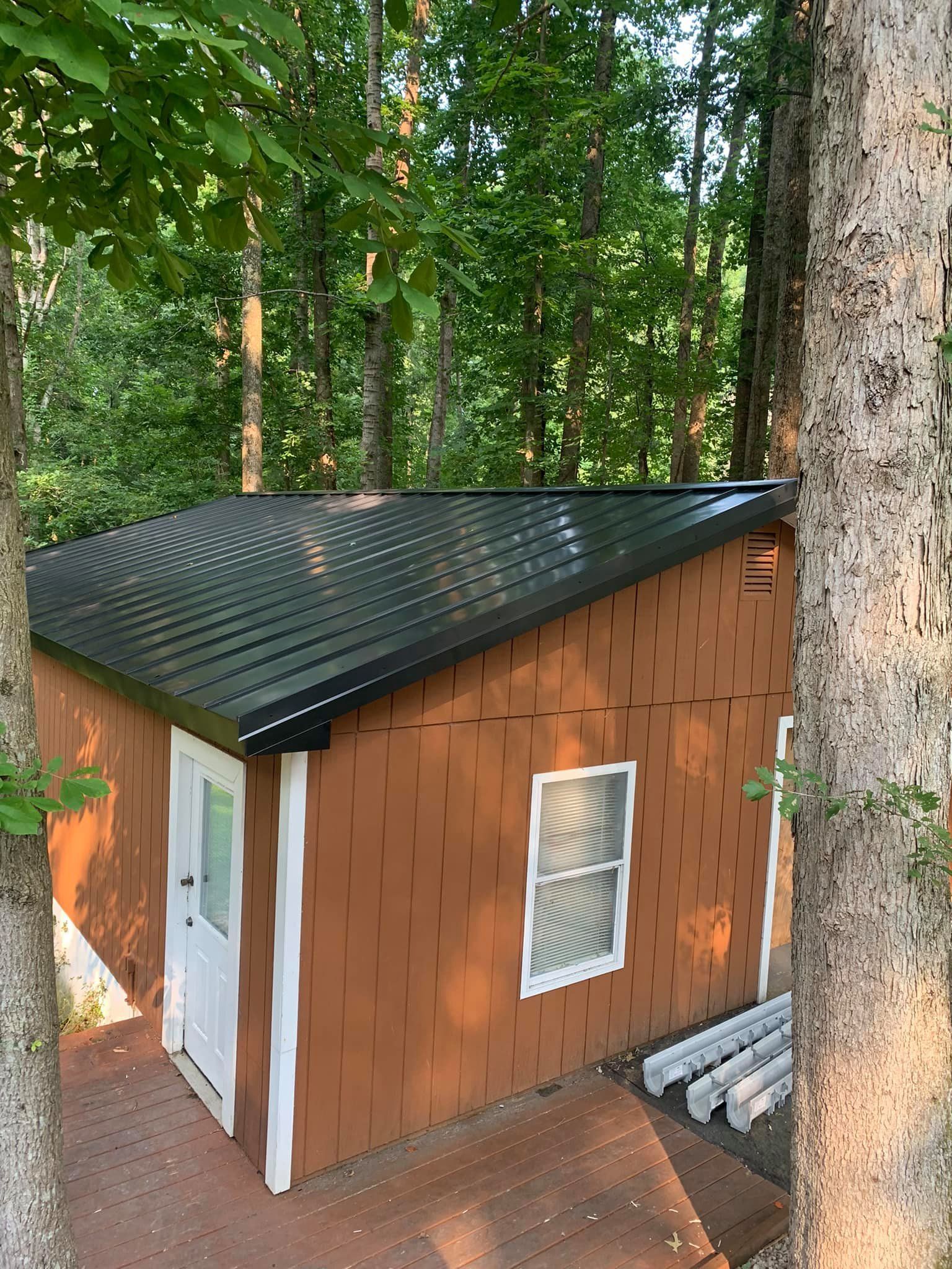 A small brown house with a black roof is surrounded by trees.