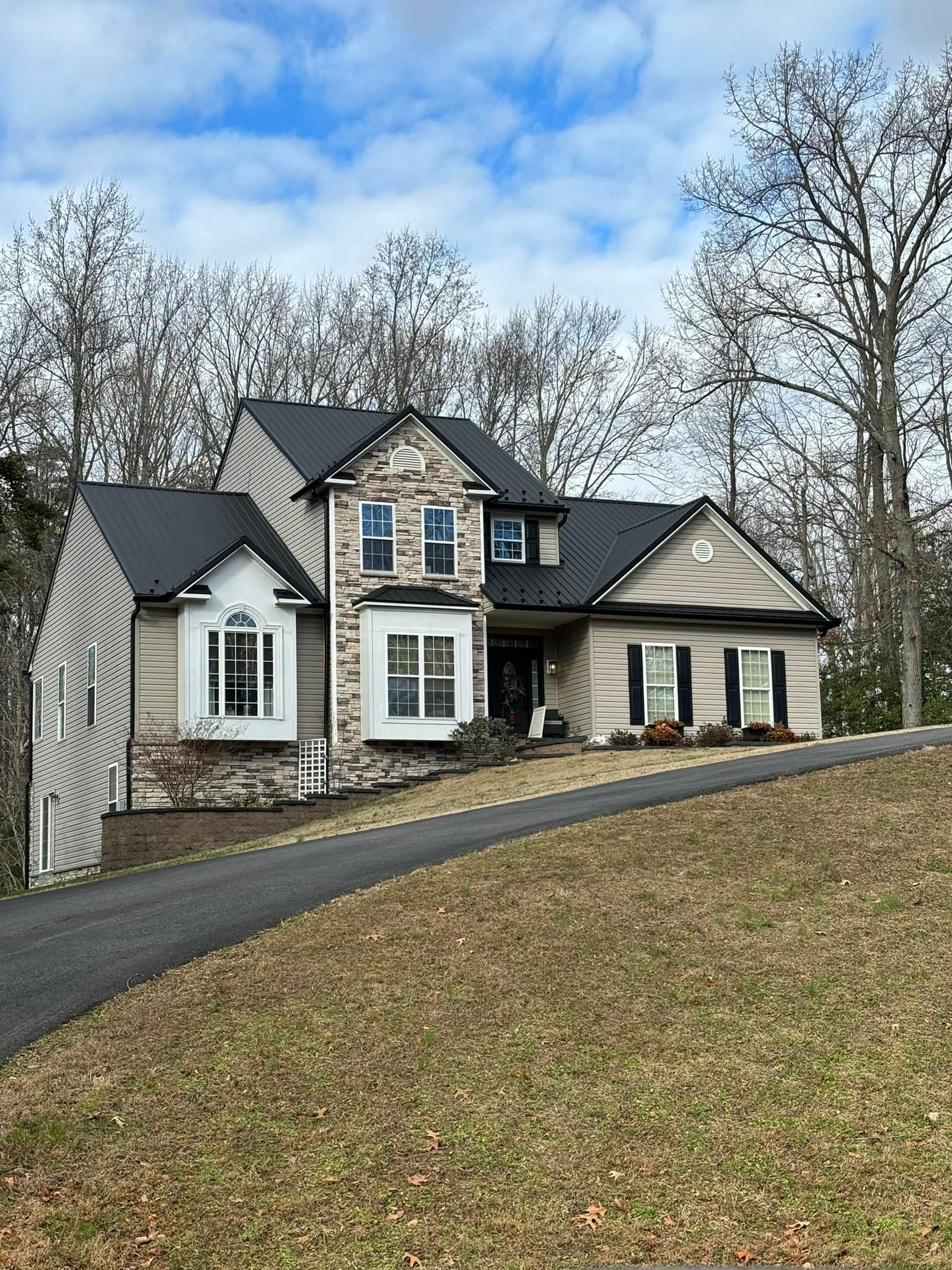 A large house with a metal black roof is sitting on top of a hill.