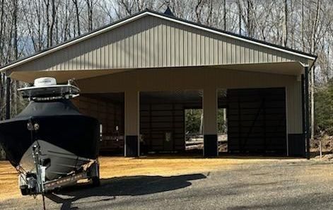 A boat is parked in front of a pole barn garage.