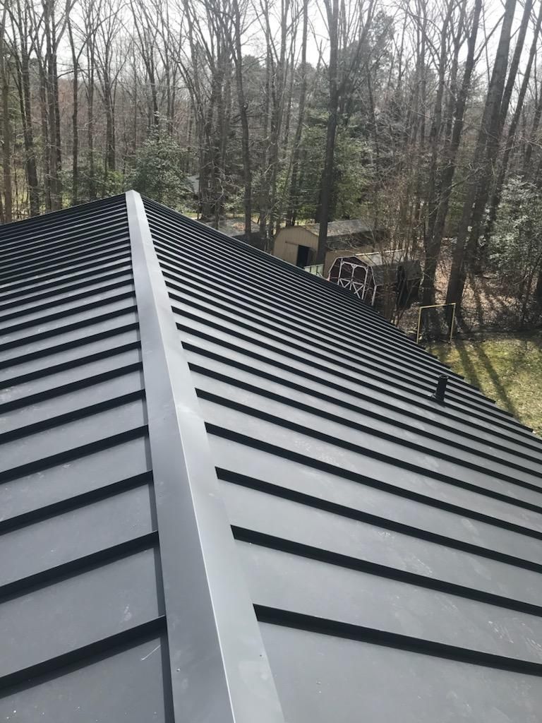 Rooftop view of dark metal standing-seam panels with trees in the background