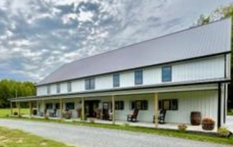 White barn with a long porch, grey roof, and a gravel driveway.