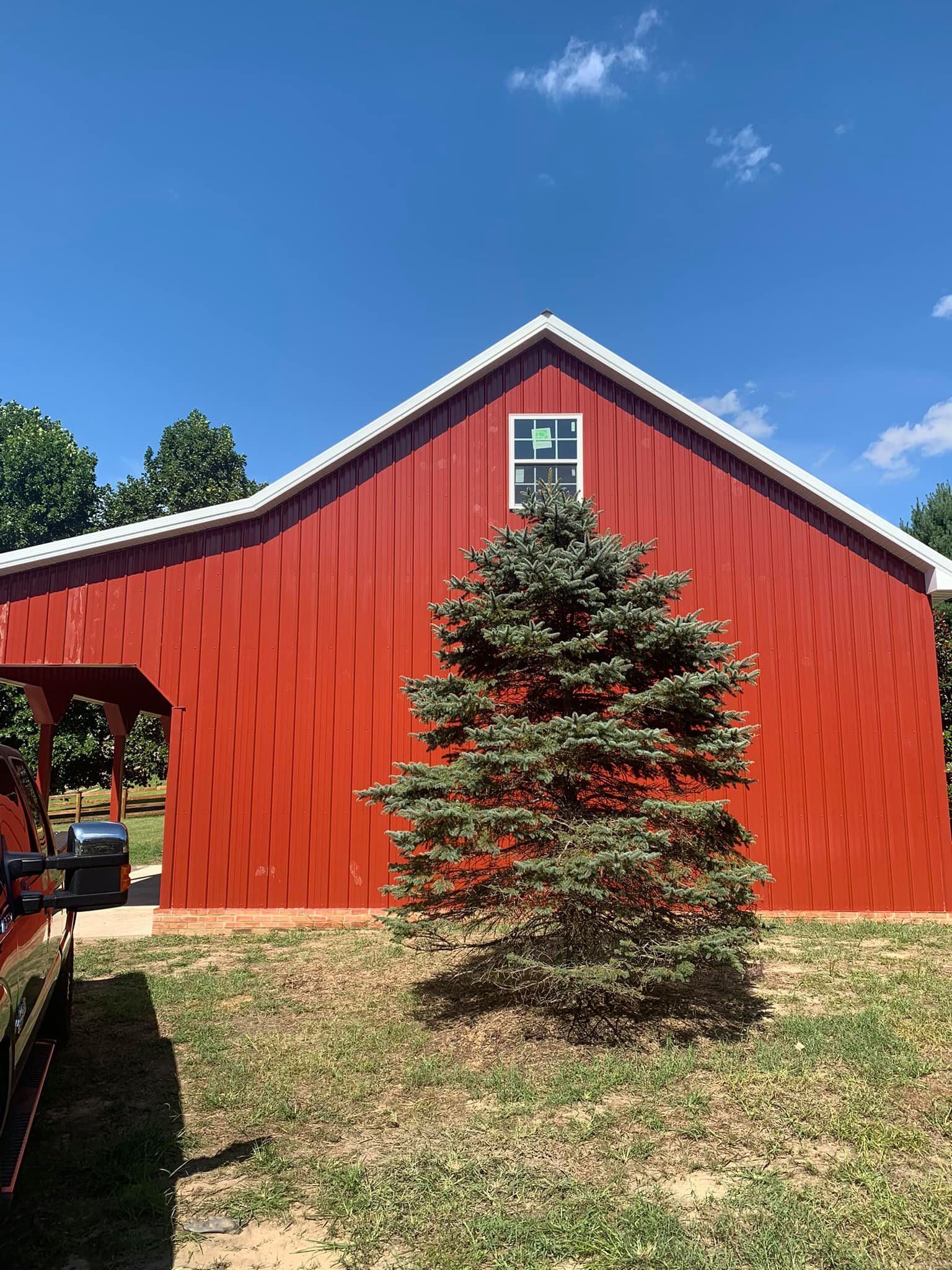 A red pole barn with a pine tree in front of it.