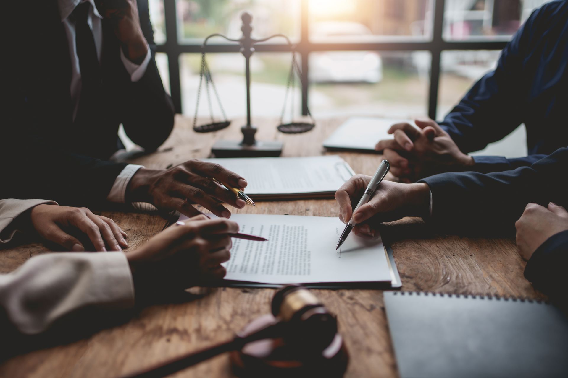 People in a meeting signing papers around a wooden table in a bright office