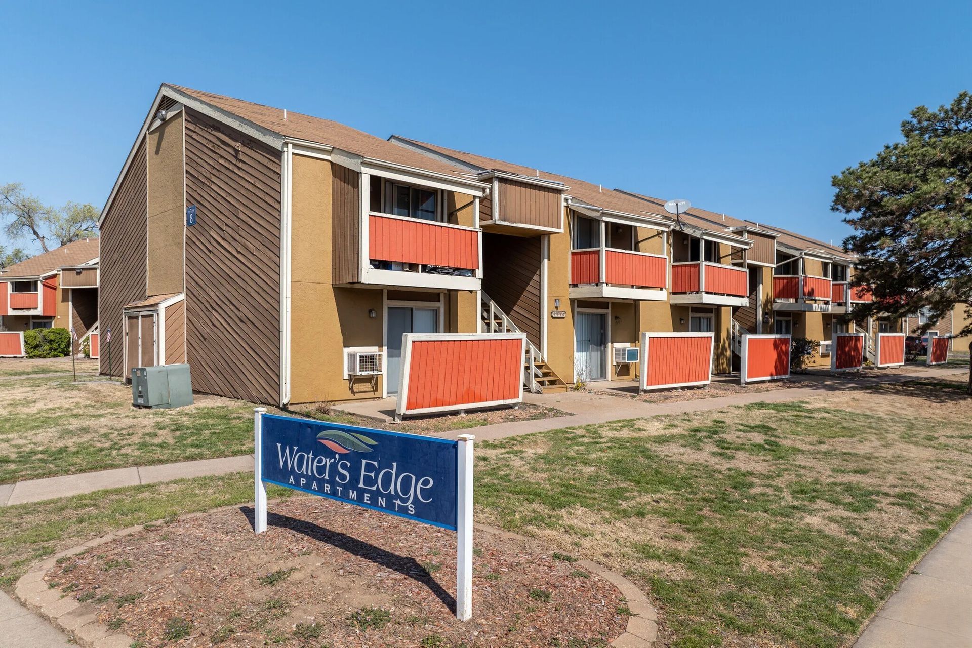 Apartment complex with orange balconies and sign that reads "Water's Edge Apartments" on a sunny day.