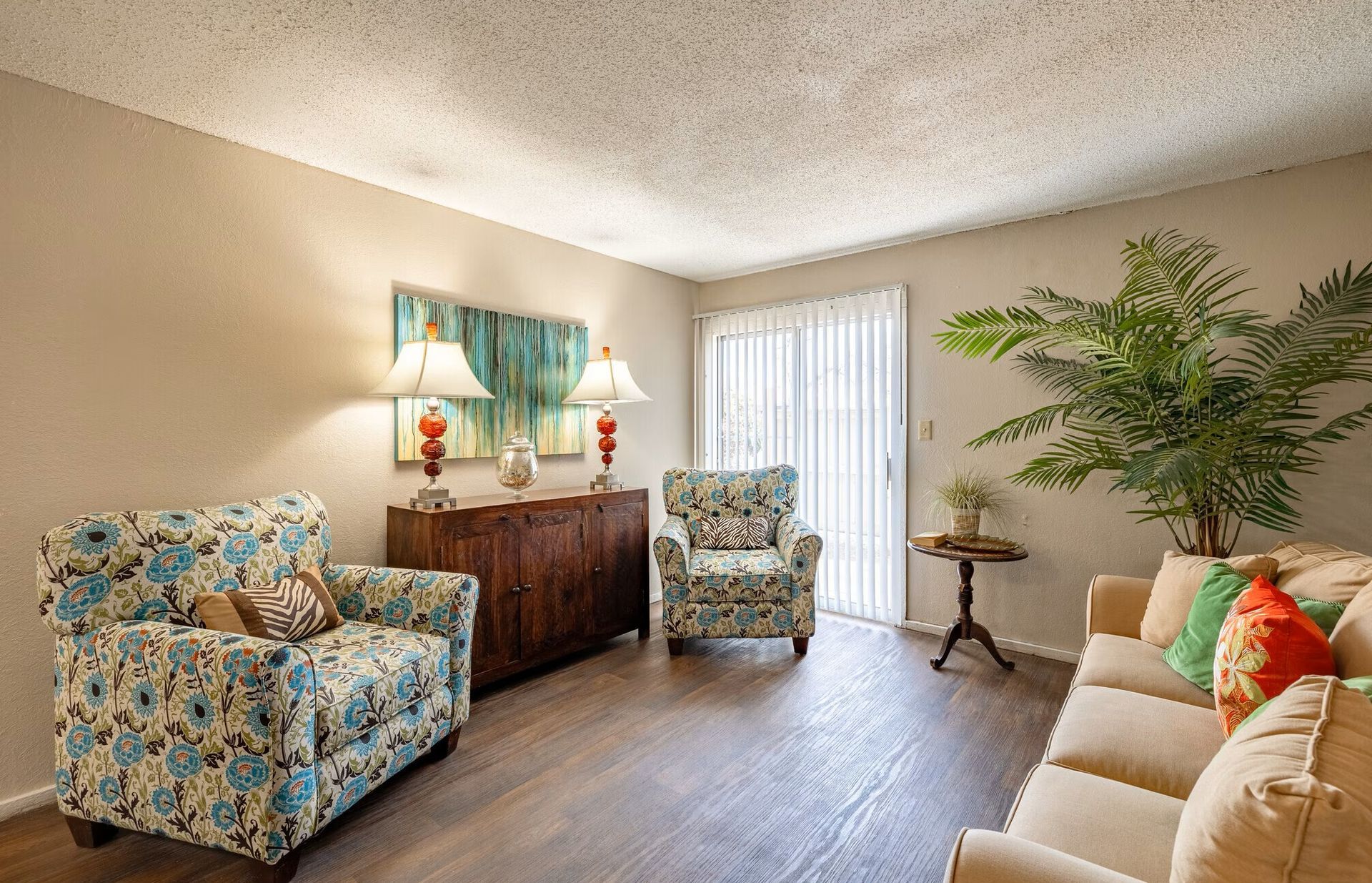 Living room with floral chairs, wooden cabinet, and sliding door.