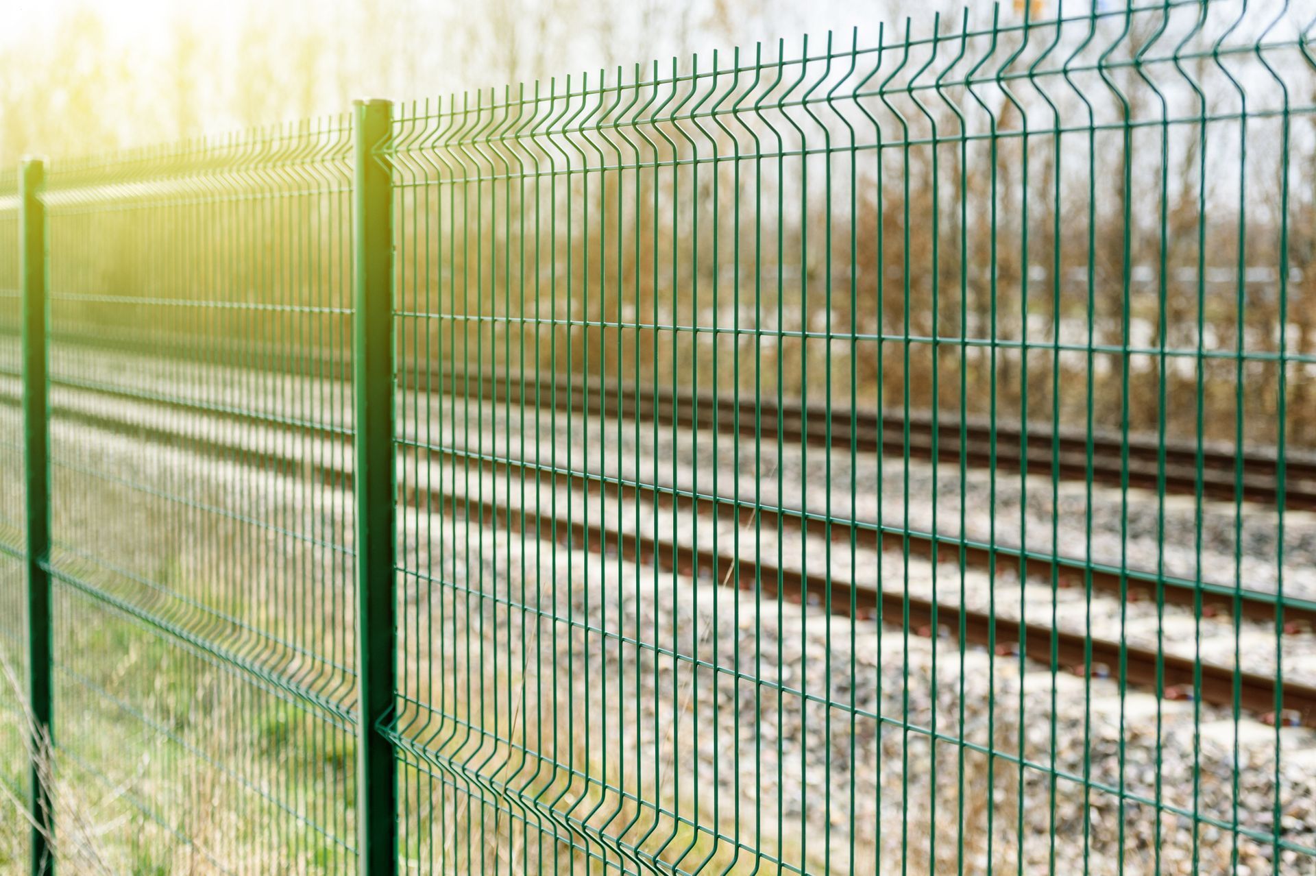 A metallic green fence is illuminated by the sun with a blurry background.