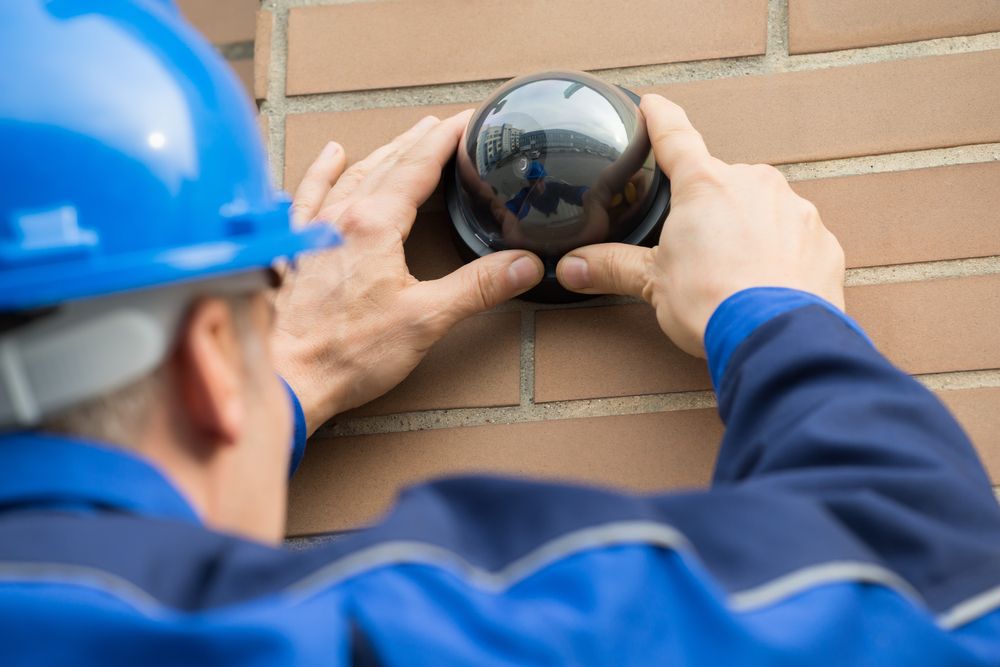 A Man is Installing a Security Camera on a Brick Wall — Direct Connect Services In Maroochydore, QLD