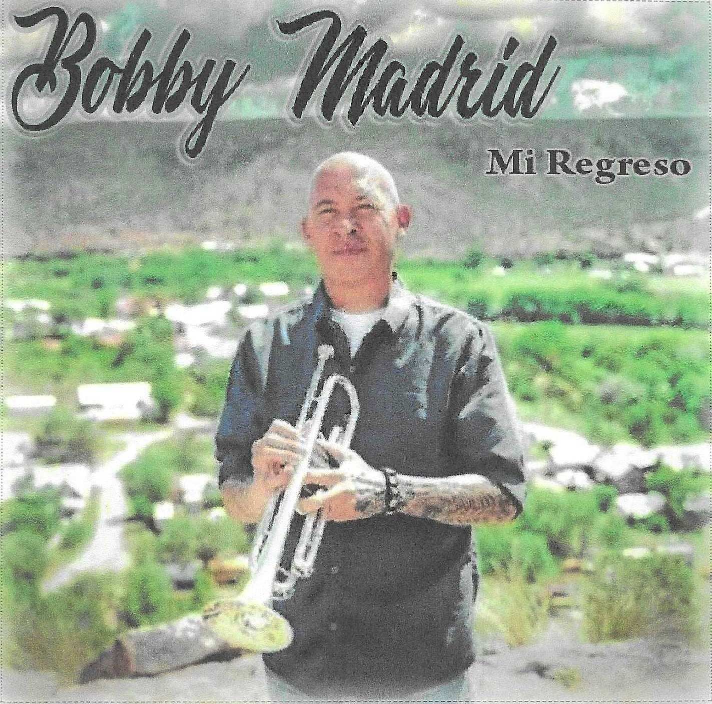 Bobby Madrid, holding a trumpet, stands outdoors with a landscape backdrop. The album title