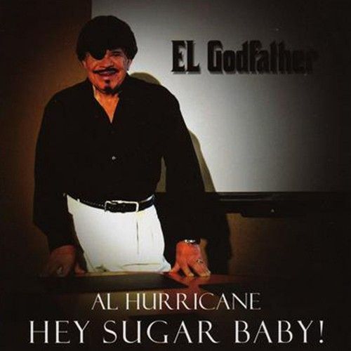 Man in black shirt and white pants, with mustache, standing next to a sign that reads