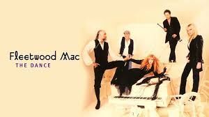 Fleetwood Mac band members, standing and seated, in black attire. The