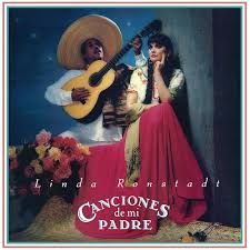 Linda Ronstadt album cover: Ronstadt with a man in a sombrero holding a guitar. They're outdoors with flowers and in front of a stone wall.