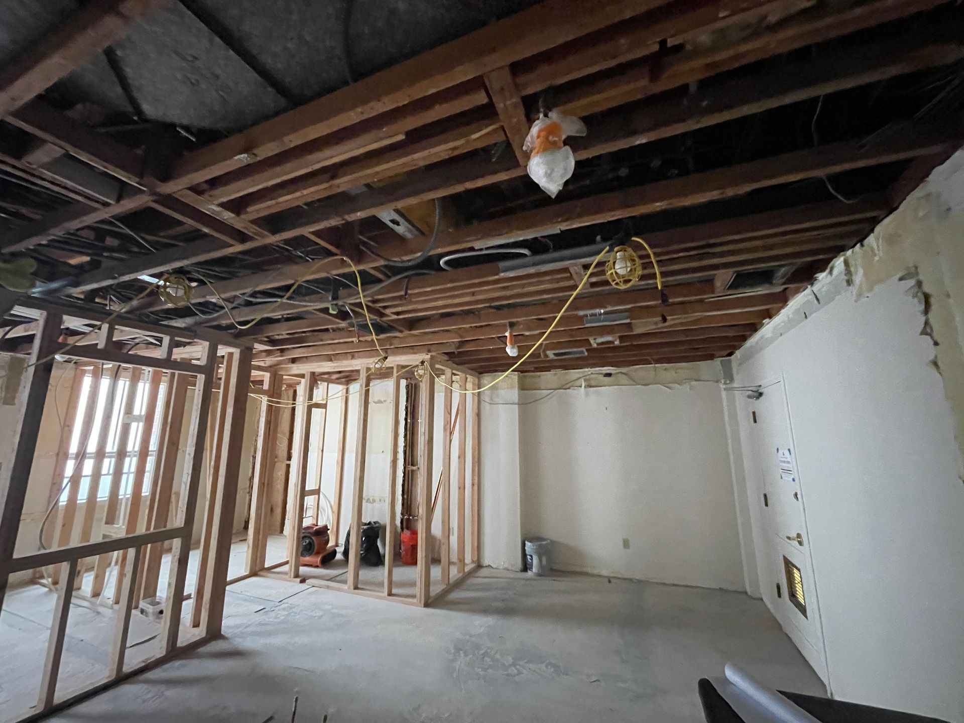 Unfinished room under renovation with exposed ceiling joists, stud walls, and drywall in progress.