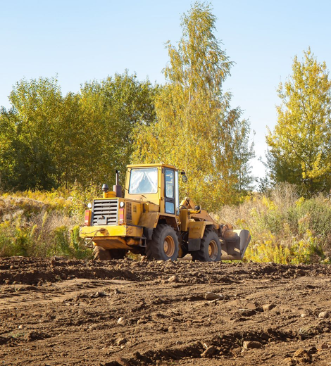Yellow bulldozer grading muddy field with trees in the background