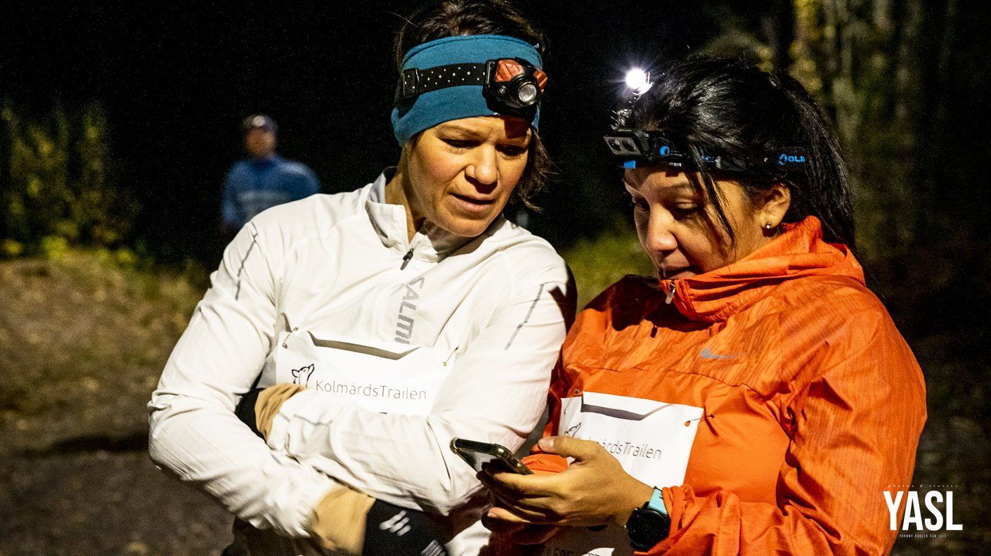 Two women wearing headlamps are looking at a cell phone.