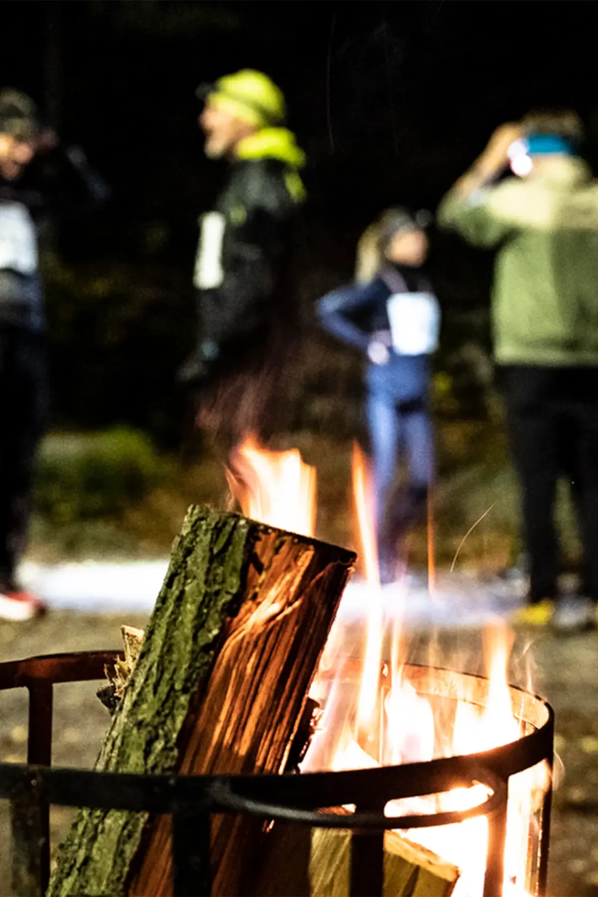 A group of people are standing around a fire pit at night.
