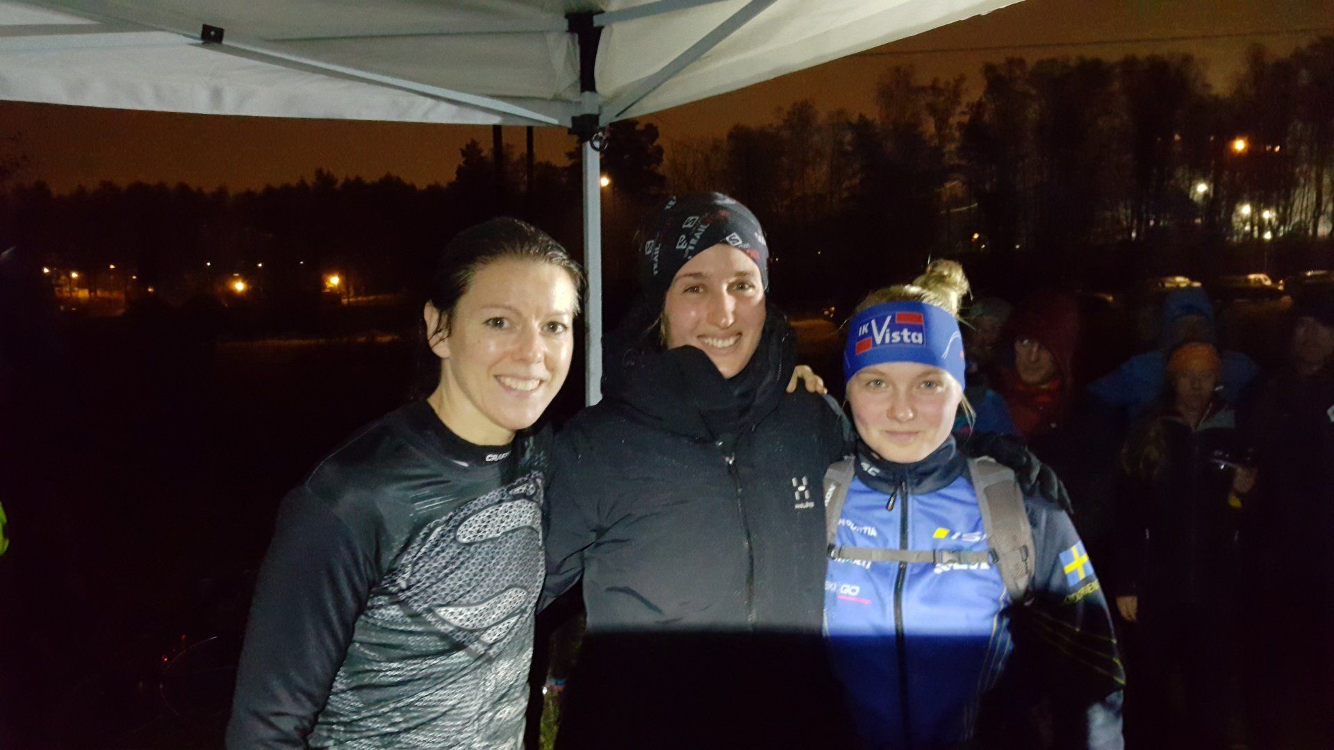 Three women are posing for a picture under a tent at night.
