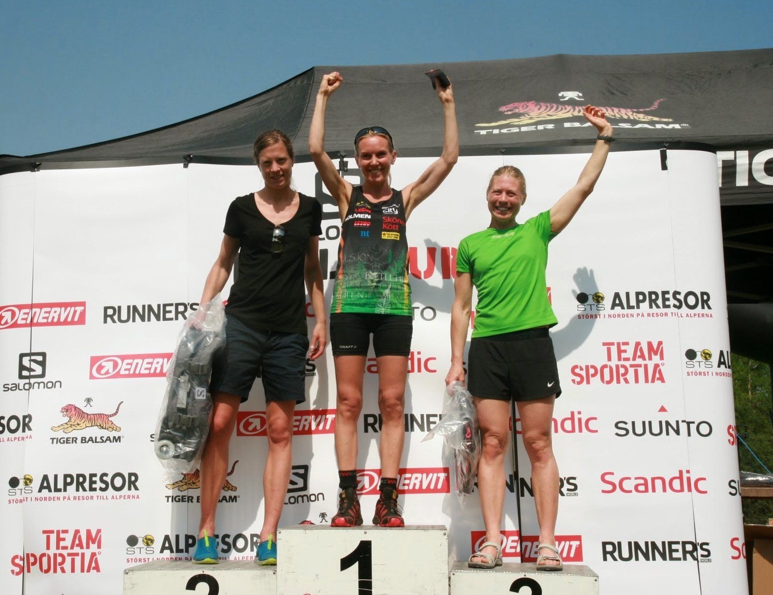 Three women stand on a podium in front of a banner that says team sportia