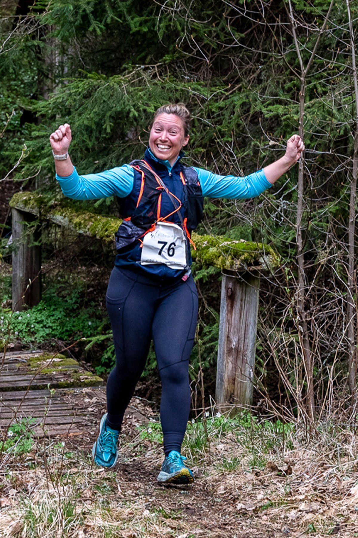 A woman is running in the woods with her arms in the air.