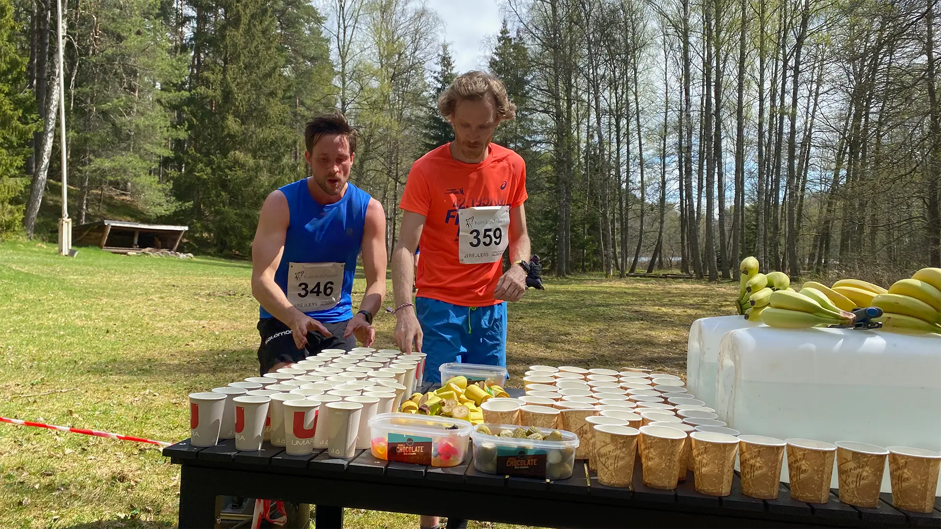 Two men are standing next to a table filled with cups of water.