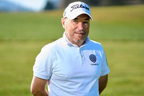 Golfer in weißem Polohemd und Kappe steht auf einem grünen Golfplatz und blickt zur Seite