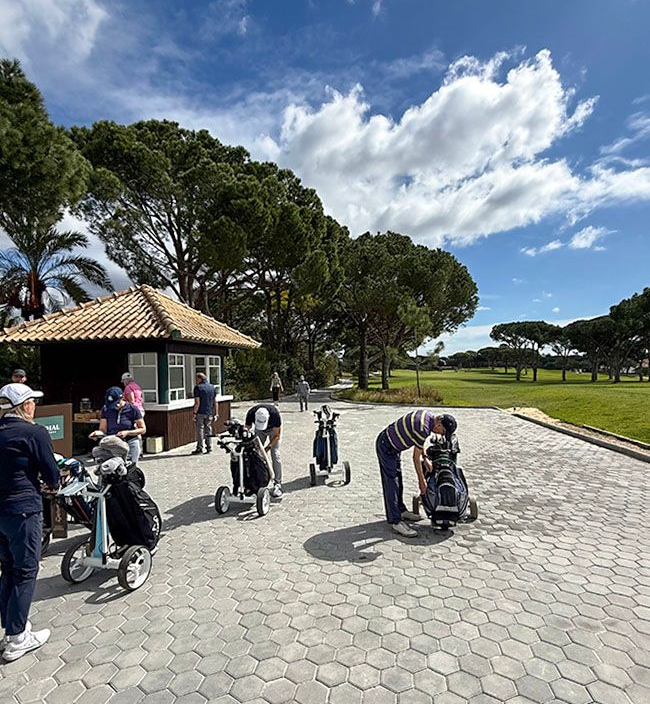 Golfer mit Golfcars auf einem sonnigen, gepflasterten Weg 