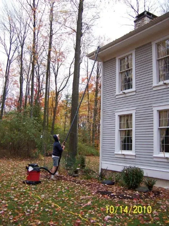 A man is cleaning the side of a house with a vacuum cleaner.